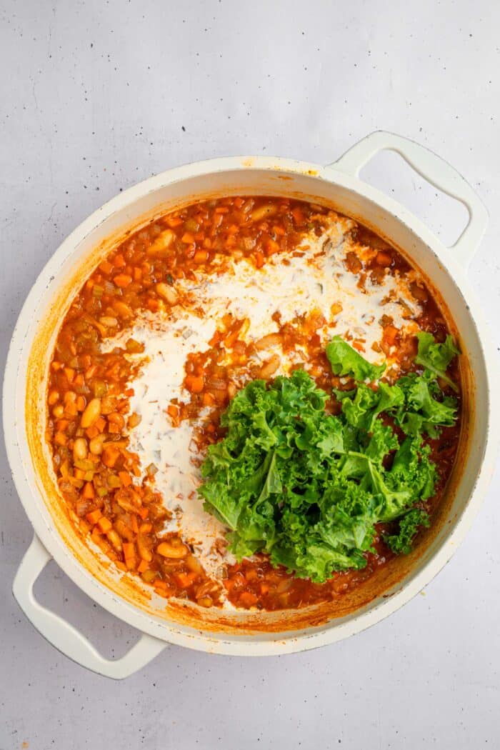 The last stage of making white bean kale soup involves adding coconut milk and kale.
