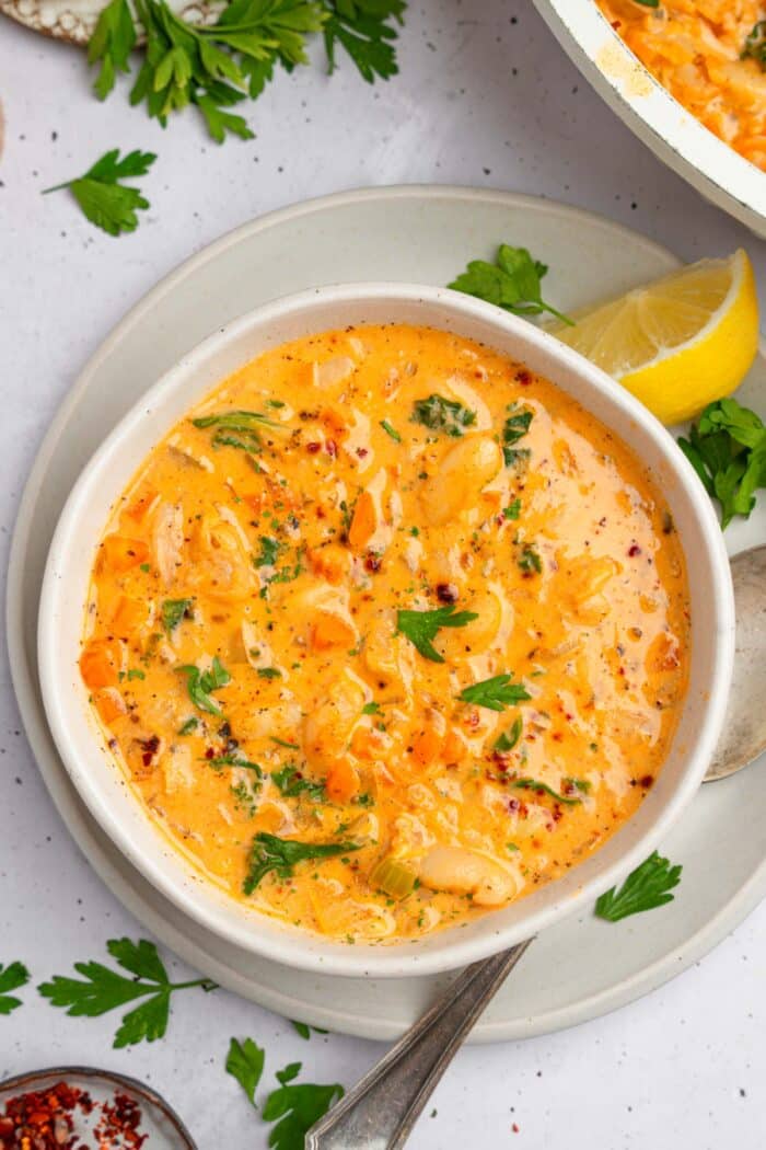 Top down view of the white bean kale soup in a white bowl, served with fresh parsley and lemon.