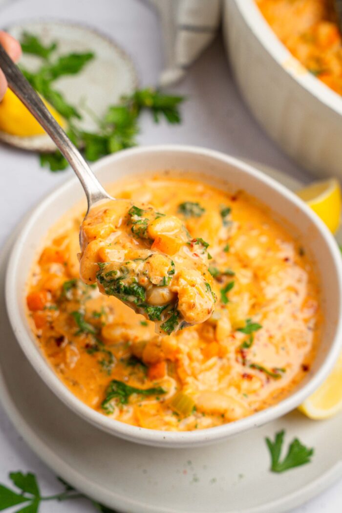 A spoonful of chunky white bean kale soup lifted into the foreground of the photo.