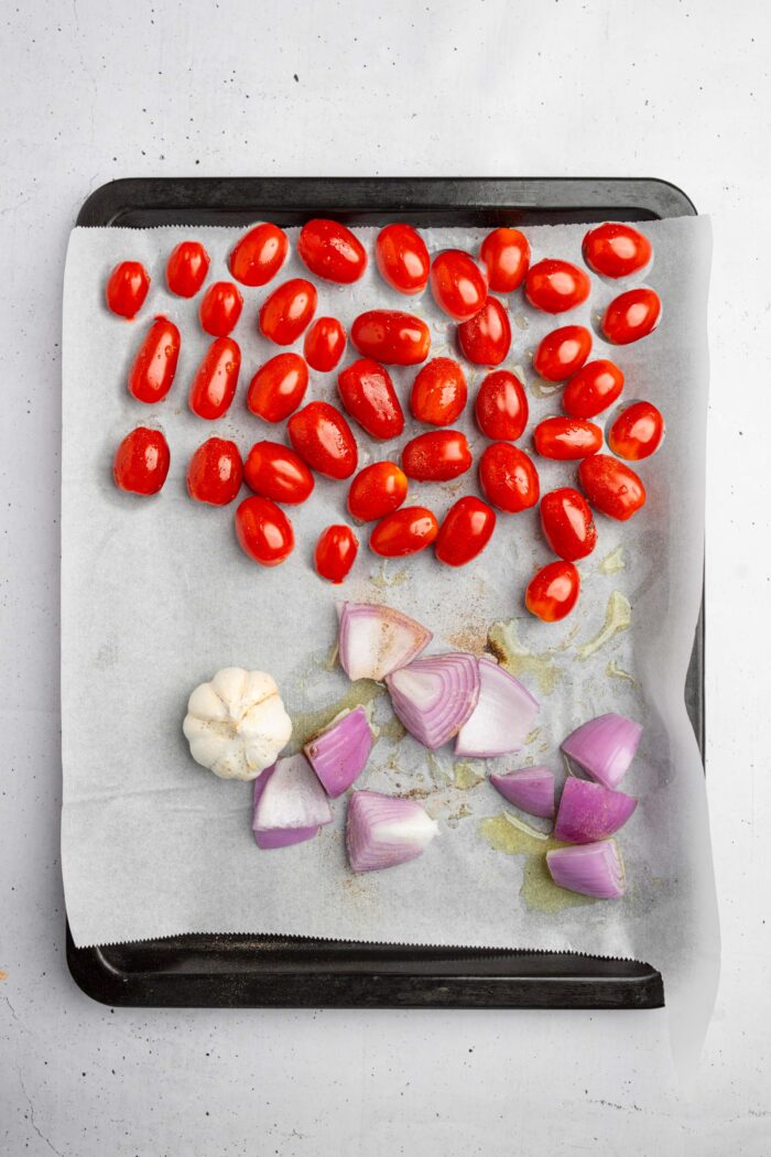 Tomatoes, garlic, and red onion on a lined sheet pan.