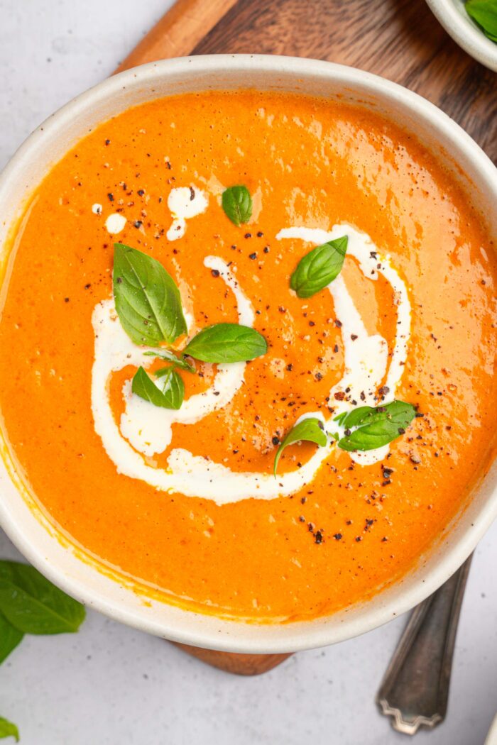 A serving of vegan high protein soup in a white cera mic bowl, with a drizzle of non dairy cream and some fresh basil.
