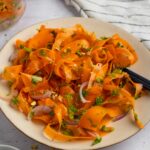 A plate full of vibrant raw carrot salad, with a jar of leftovers visible in the background.