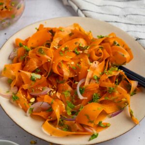 A plate full of vibrant raw carrot salad, with a jar of leftovers visible in the background.