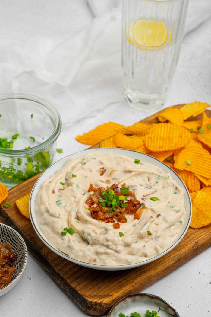 A broad view of a bowl full of caramelized onion dip on a cutting board with chips for dipping.