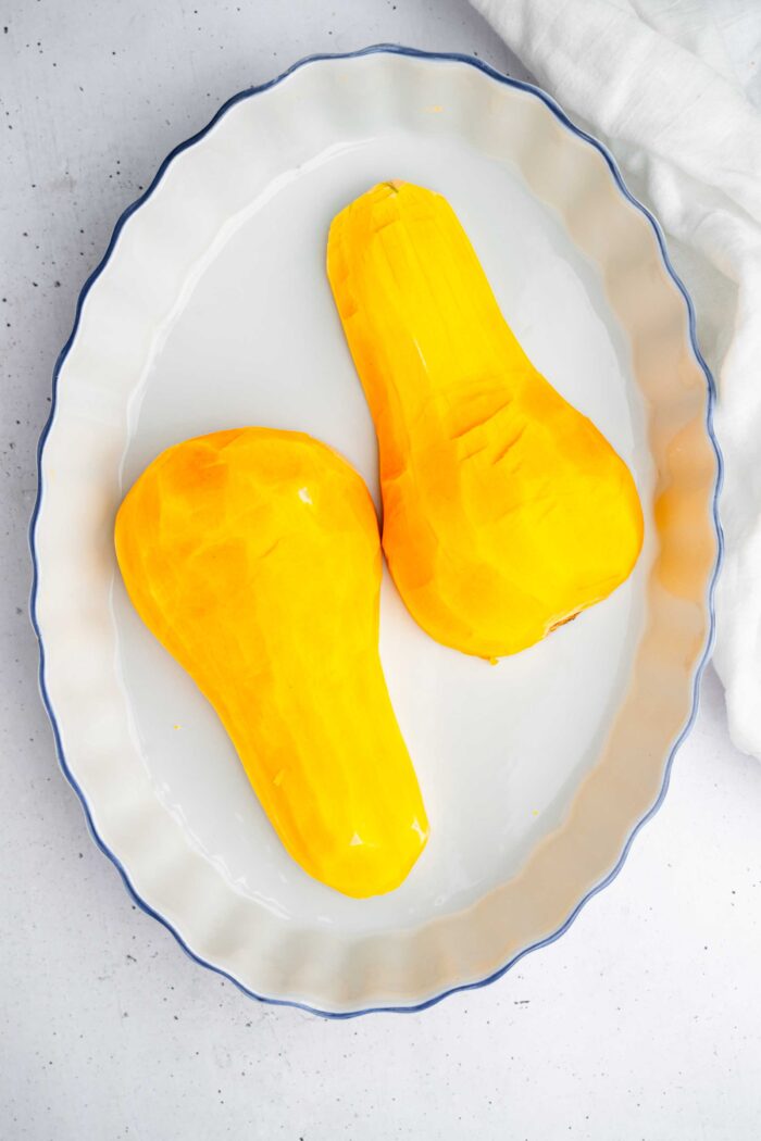 Peeled butternut squash cut in half and placed into a roasting dish.