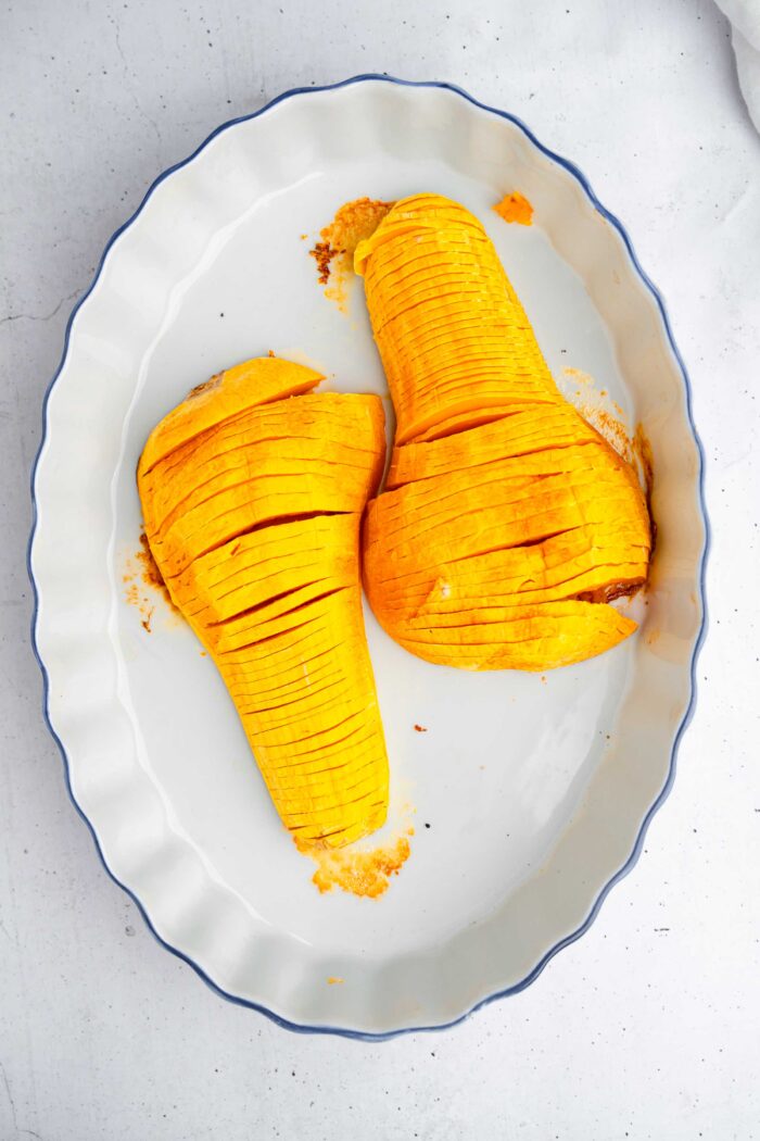 Hasselback butternut squash laid out in the roasting pan, with thin slices of garlic between the slits.