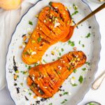 Hasselback butternut squash served on an oval platter with chopped pistachios and fresh parsley.