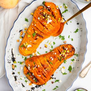 Hasselback butternut squash served on an oval platter with chopped pistachios and fresh parsley.