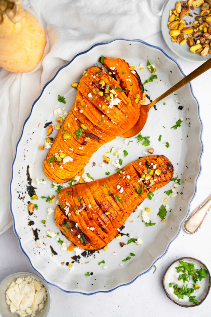 Hasselback butternut squash served on an oval platter with chopped pistachios and fresh parsley.