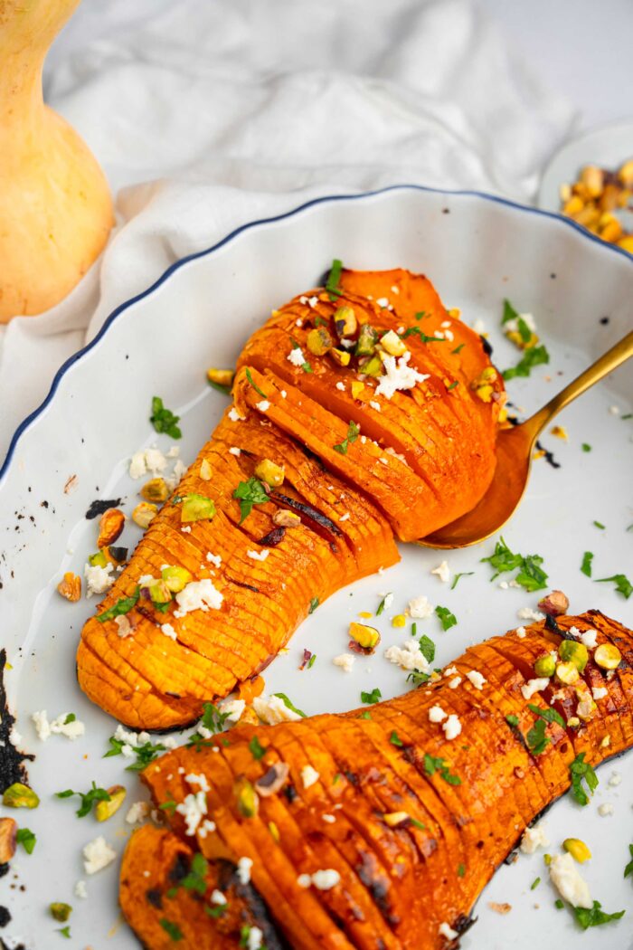 A gold-tinted spoon picking up half of the hasselback butternut squash to show it off.