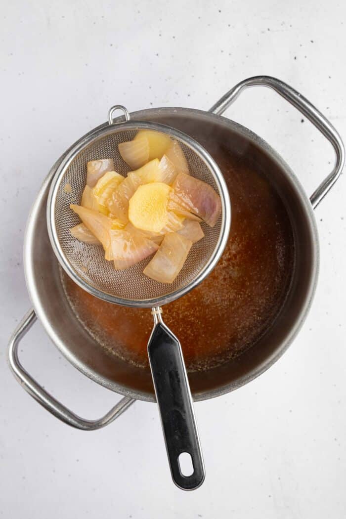 A sieve with strained broth ingredients above the strained infused ramen broth.