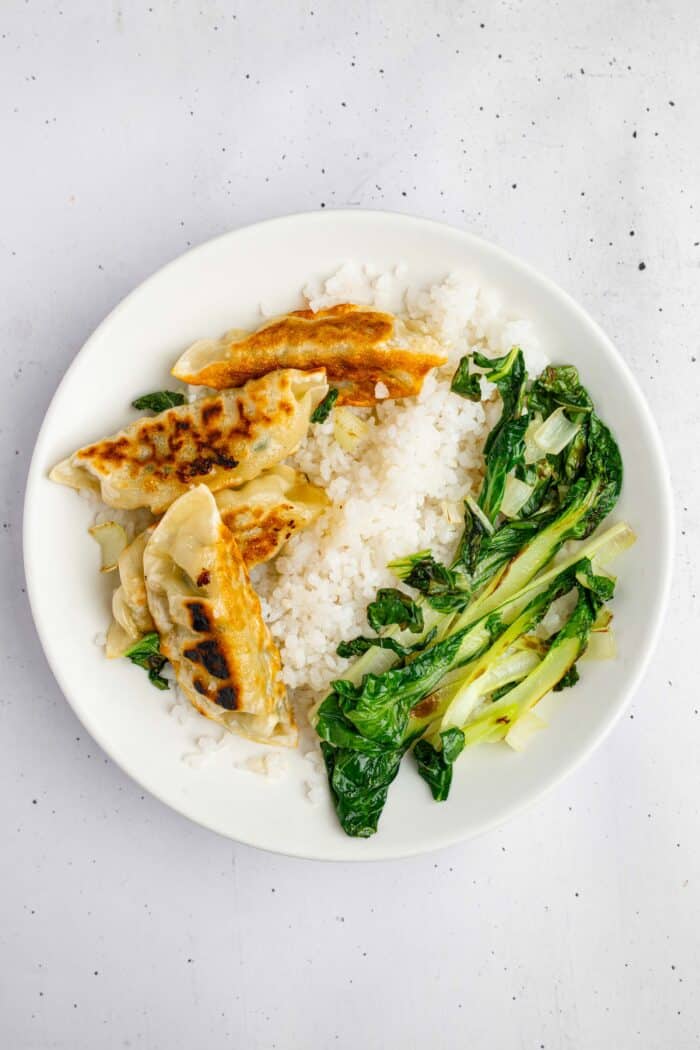 Rice, fried dumplings and bok choy laid out in a white bowl.