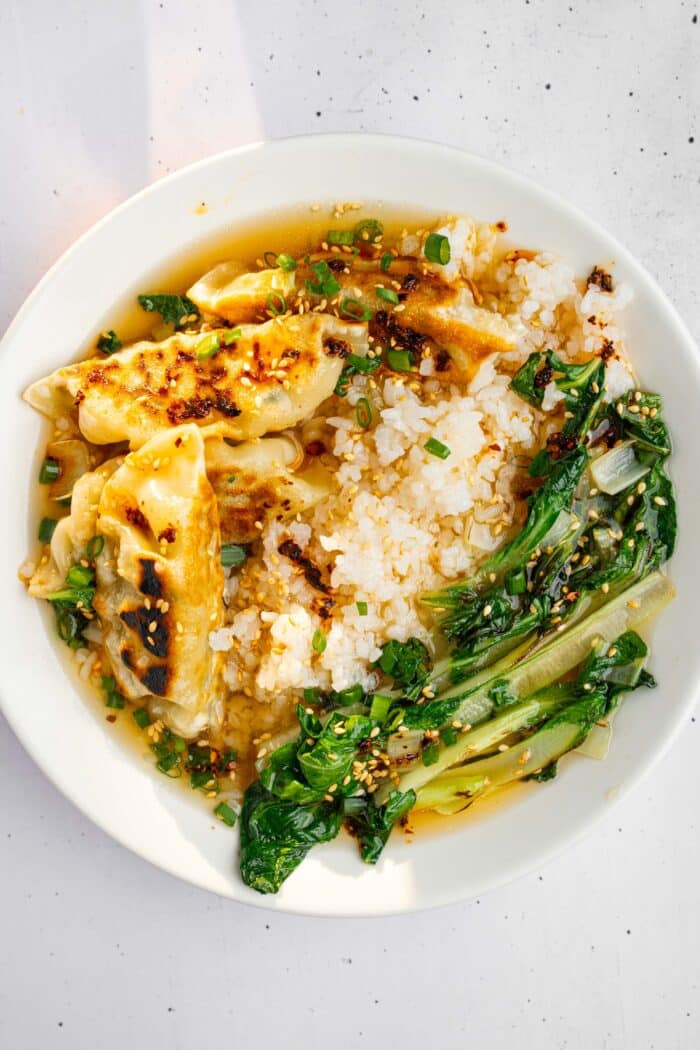 Broth poured over a serving of rice, bok choy, and fried vegan dumplings.