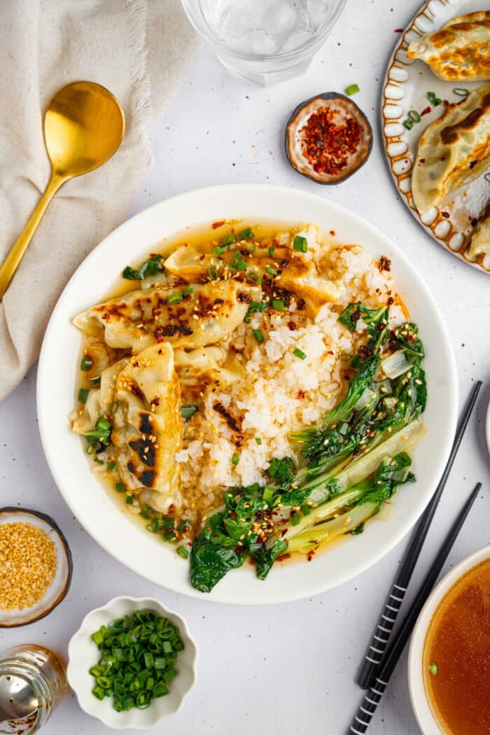 A title image showing steamed rice, sauteed bok choy and fried dumplings served with aromatic broth in a white ceramic bowl.