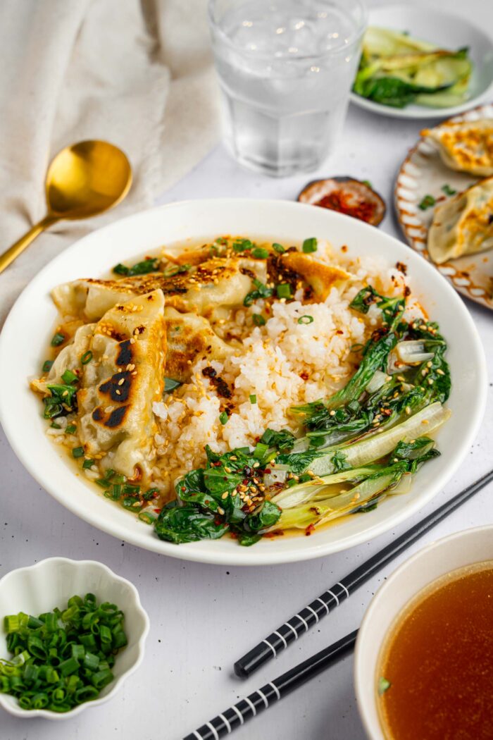 A big bowl of brothy rice with ginger and garlic with fixings visible in the picture background.
