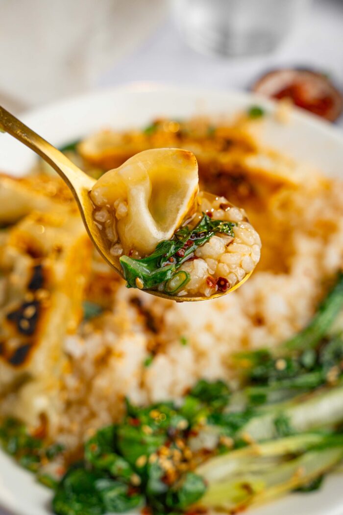 A spoonful of brothy rice with ginger and garlic lifted to the foreground, with the rest of the bowl visible in the background.