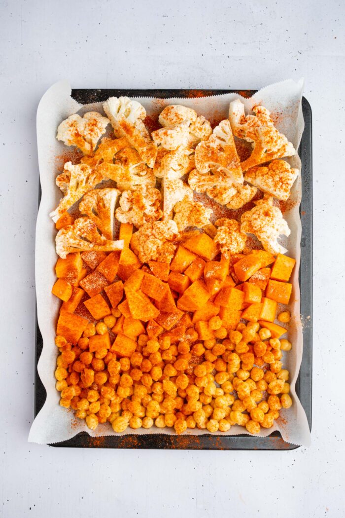 Cauliflower, sweet potato, and chickpeas tossed with spices and laid out on a baking tray.