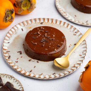 A serving of persimmon pudding on a ceramic plate, with a golden spoon to serve.