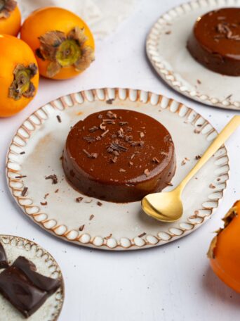 A serving of persimmon pudding on a ceramic plate, with a golden spoon to serve.