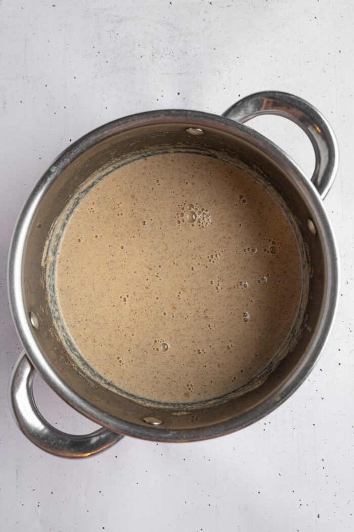 Warm date milk whisked in a steel saucepan to create a spiced mixture.