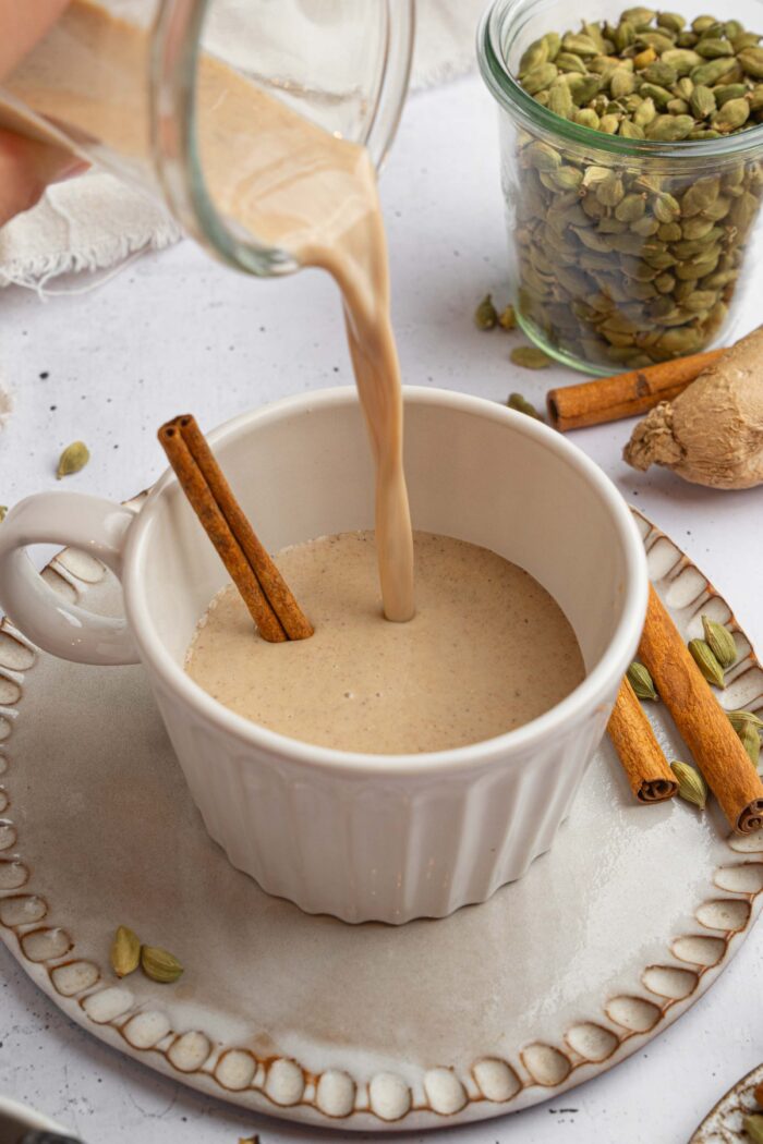 Warm date milk being poured into a mug with a cinnamon stick sticking out.