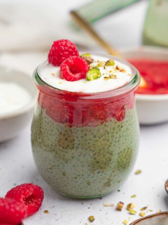 Matcha chia pudding served with fresh raspberries and pistachios in a seethrough jar.