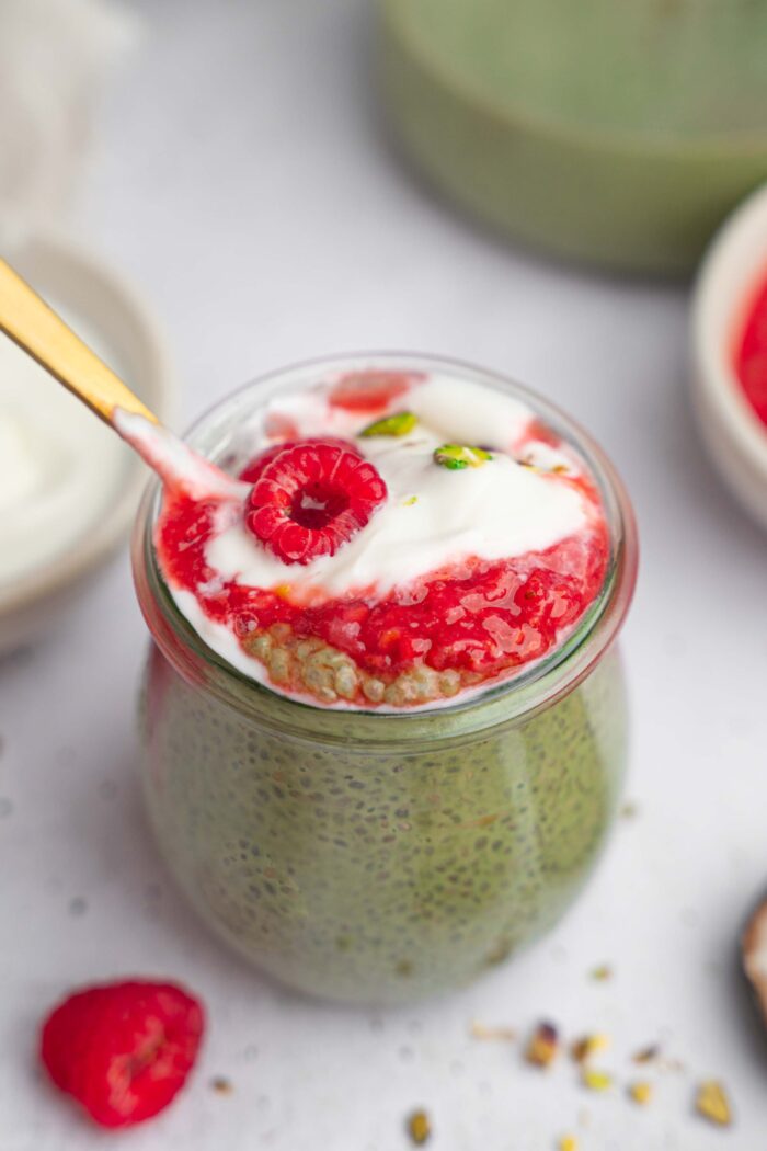 A spoon sticking out from the matcha chia pudding and lifting all the layers at the same time.