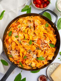 One pot creamy vegan pasta in a large skillet, with vegan parmesan and fresh basil as garnish.