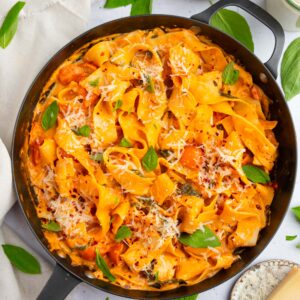One pot creamy vegan pasta in a large skillet, with vegan parmesan and fresh basil as garnish.