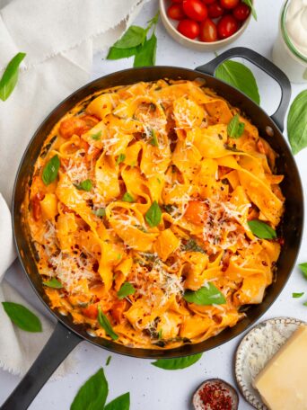 One pot creamy vegan pasta in a large skillet, with vegan parmesan and fresh basil as garnish.