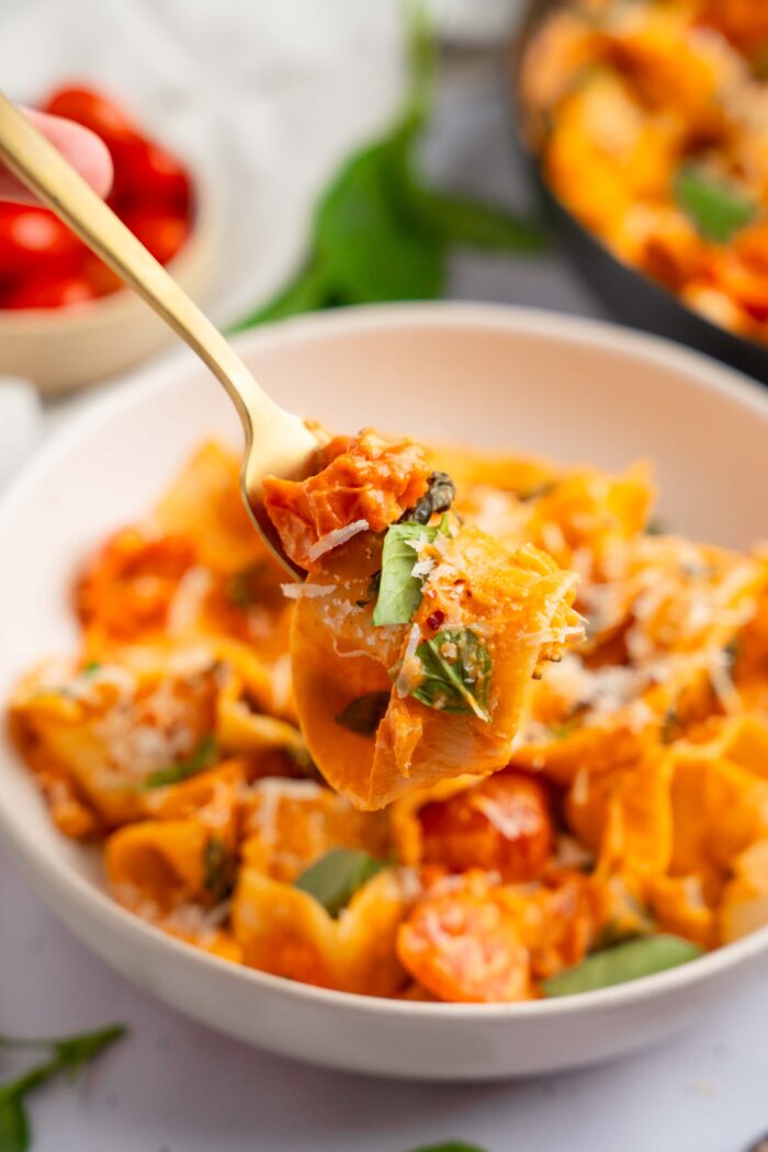 A fork carrying some creamy vegan pasta in the foreground, with the rest of the serving visible in the background.