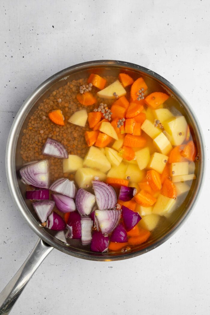 A deep frying pan, filled with lentils, potatoes, carrot, and onion.