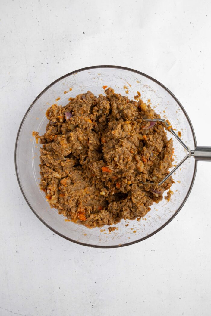 Lentils and vegetables mashed together with a potato masher.
