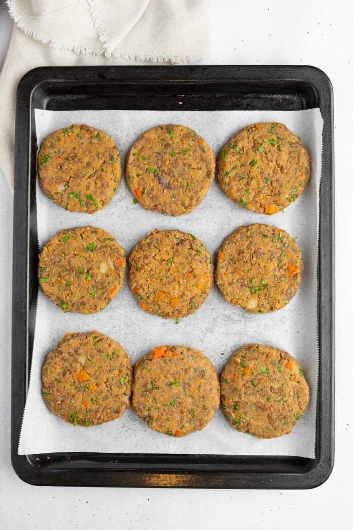 Lentil patties rolled out and laid out on a lined baking sheet side by side.