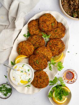 Lentil patties served on a big platter with a creamy vegan dip on the side and some lemon wedges.