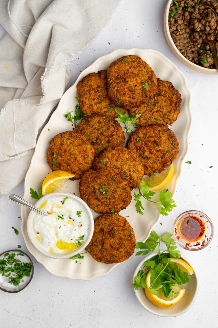 Lentil patties served on a big platter with a creamy vegan dip on the side and some lemon wedges.