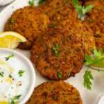 Closer shot of the lentil patties with some fresh herbs and a creamy vegan dip.