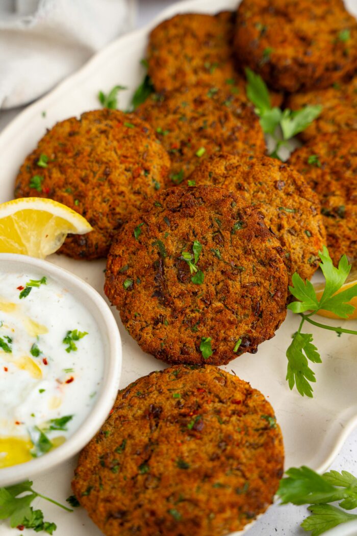 Closer shot of the lentil patties with some fresh herbs and a creamy vegan dip.