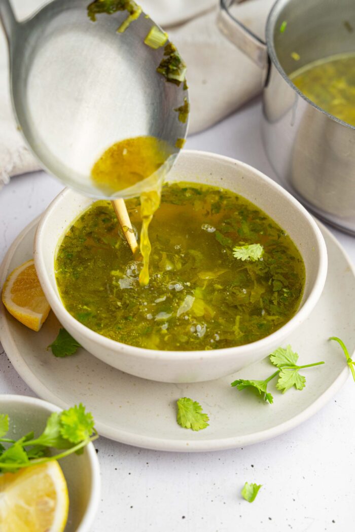 A serving of cilantro lemon soup being poured into the bowl using a ladel.