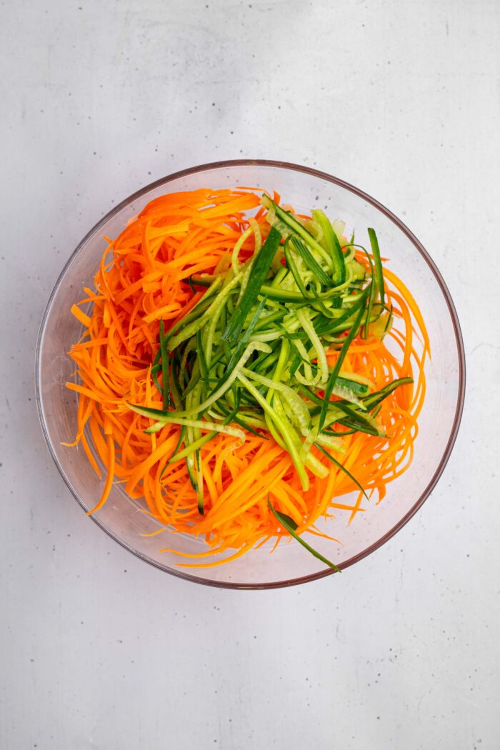 Spiralized carrots and cucumber in a large glass bowl.