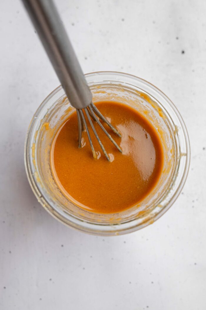 A whisk sticking out of a bowl with peanut lime dressing.
