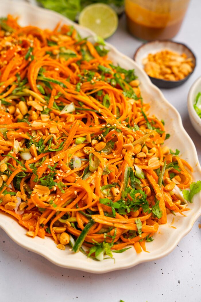 A closer shot of carrot and cucumber salad with additiona like peanuts and lime visible in the background.