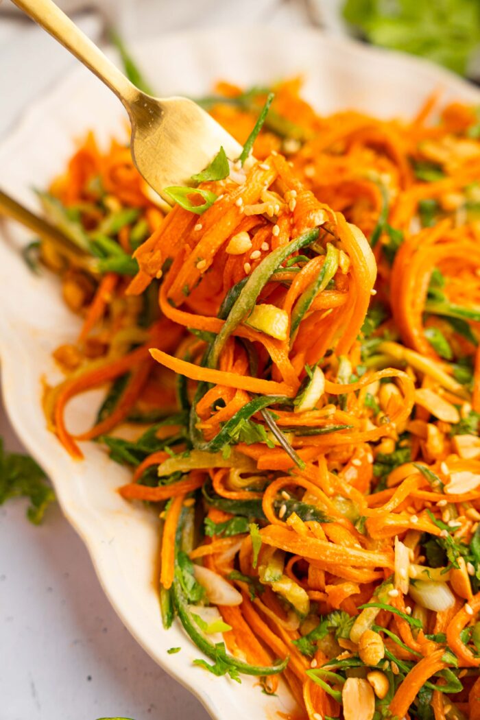 A close up of a fork carrying some carrot and cucumber salad like spaghetti.