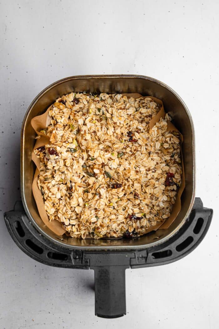 The granola mixture added to the lined air fryer drawer.
