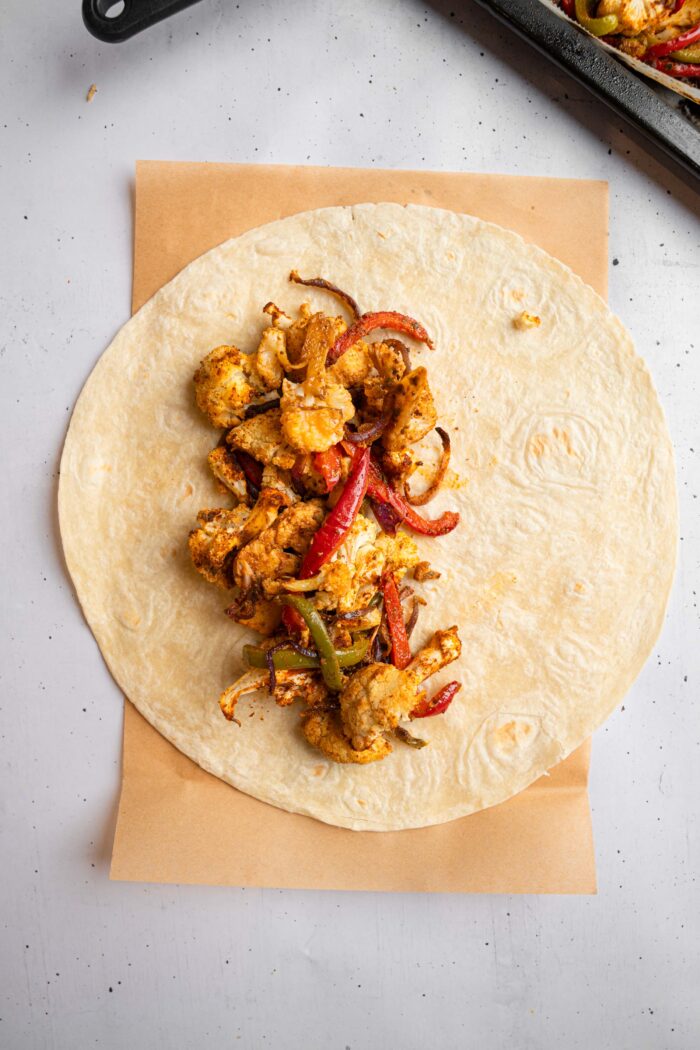 A warmed up tortilla laid out with some vegetable filling piled in the middle.