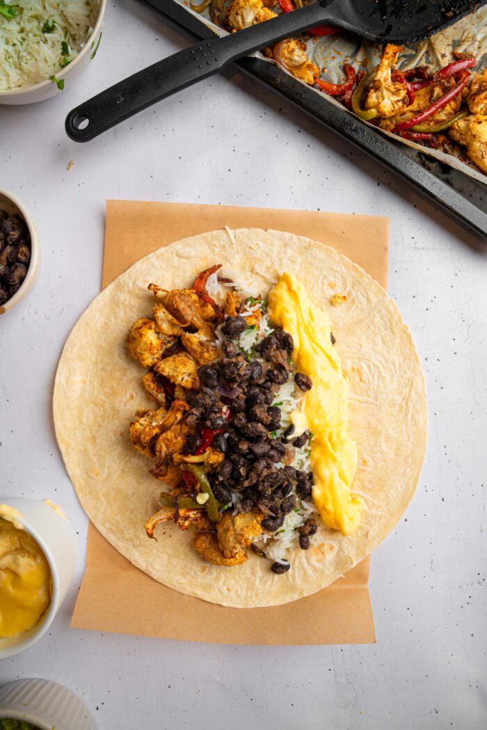 Beans, vegan queso, and rice added to the vegetable mixture in the tortilla.