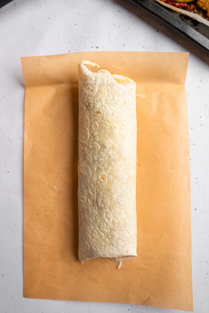 A neatly wrapped cauliflower burrito on a piece of parchment paper.