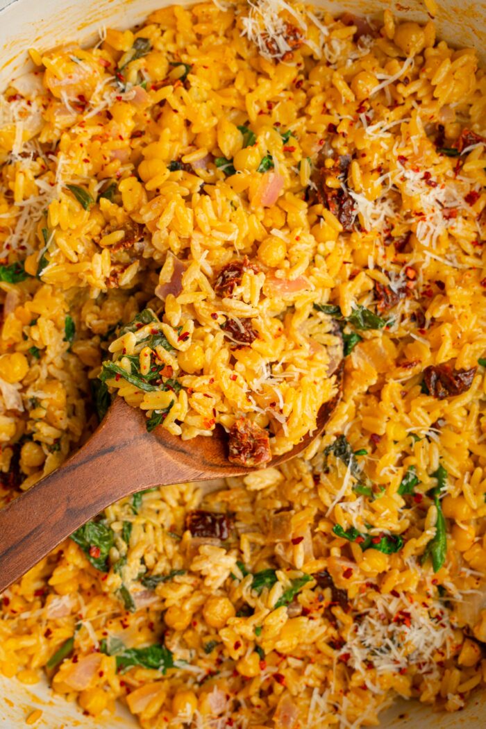 A wooden spoon scooping some marry me orzo to serve it after cooking.