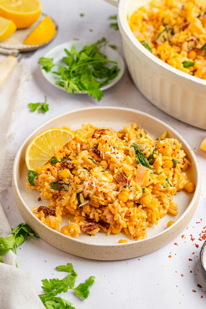 A serving of marry me orzo with fresh herbs and a lemon wedge in a shallow bowl.