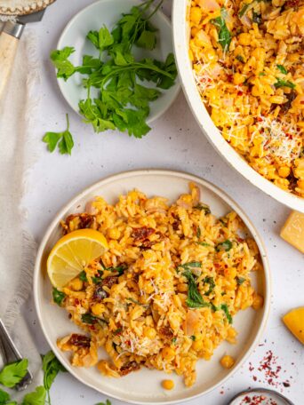 A serving of marry me orzo in a shallow bowl, with the rest of the dish still in the pan, visible in the upper corner.
